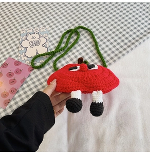 Macro shot of handmade crochet red apple bag with funny cute eyes and hanging legs