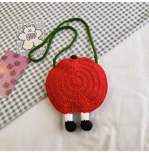 Close-up detail of a handmade crochet apple bag with green straps and cute feet decor