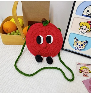 Detailed view of a handmade red knitted apple coin purse with cartoon eyes and green strap