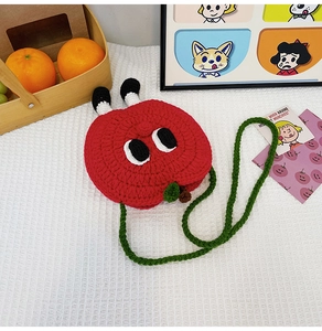 Detail of red apple crochet crossbody bag featuring cartoon eye accents and green strap