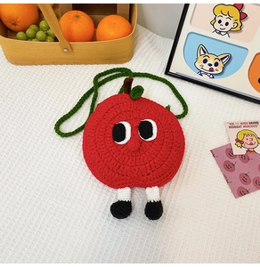 Close-up of a red knitted apple-shaped mini bag with cute cartoon eyes and woven strap