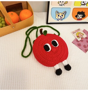 Close-up of handmade red apple crochet mini bag with cartoon eyes and 3D legs