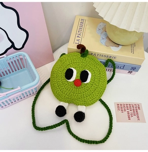 Close-up of handmade green knitted apple bag with cartoon eyes and woven shoulder strap