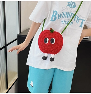 Close-up of a handmade red apple knitted crossbody bag with cartoon eyes and green straps