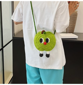 Detail showing a green knitted apple-shaped mini bag with cute cartoon character eyes