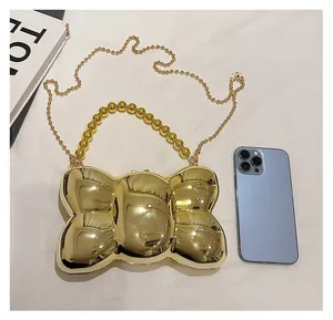 Détail de la pochette dorée en forme de nœud avec poignée perlée et chaîne près d'un mobile