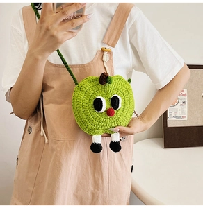 Close-up of green hand-knitted apple coin purse with cute cartoon eyes and legs