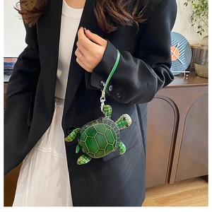 Détail du mini sac tortue verte avec coque texturée porté par un mannequin à la main