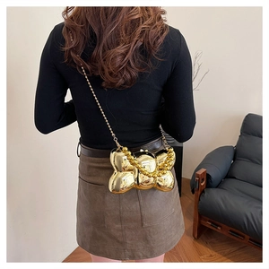 Vue détaillée de la pochette dorée en forme de nœud avec chaîne à billes sur mannequin