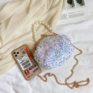 Iridescent sequin shell bag with large pearl handle and gold chain strap in a lifestyle set