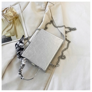 Detail of silver box clutch with metallic texture, chain strap, and silk scarf handle