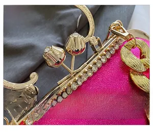 Detailed close-up of rose pink glossy evening bag with floral gold clasp and crystal trim