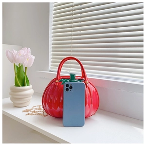 Mini red pumpkin-shaped patent leather handbag with gold chain shown with smartphone for size