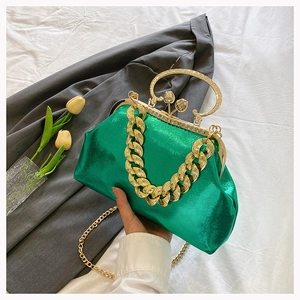 Detailed shot of emerald green glossy shell bag with bold gold chain and floral metal clasp