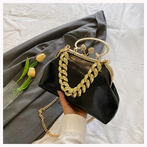 Detail of black evening bag featuring a gold chunky chain handle and floral decorative clasp