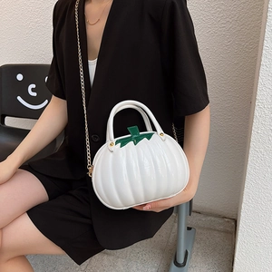 White pumpkin-shaped handbag with green leaf handle and gold chain strap on model