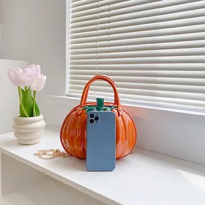Orange pumpkin shaped handbag with green leaf decor and gold chain shoulder strap