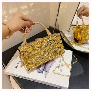 Detalle de bolso de fiesta dorado con textura de grietas, asa de metal y cadena