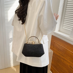 Sparkly black evening bag with gold handle and pearl clasp on a white suit model