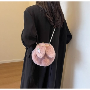 Detail of pink plush rabbit crossbody bag with pearl strap on model's black coat