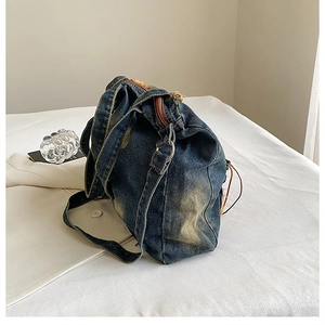 Detail of blue washed denim tote bag with metal buckle and smooth zipper closure