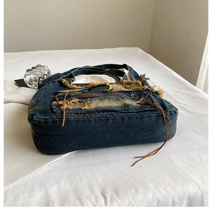 Detail of distressed dark blue denim bucket bag with frayed edges and brown ties