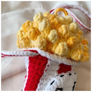 Detail of a handmade popcorn-shaped crochet bag with red and white stripes and yellow wool