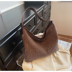 Dettaglio borsa a secchiello in camoscio marrone con strass argento su mobile in legno