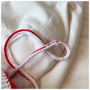 Detail of red and white handmade crochet knit texture on a crossbody popcorn bag strap
