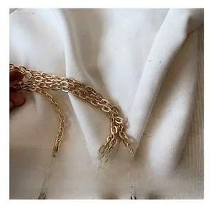 Macro view of three-layered polished gold metal chain strap on minimalist cylinder bag