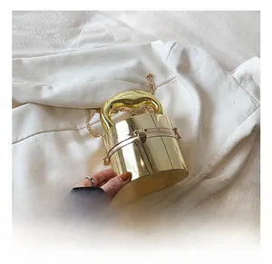 Macro detail of glossy golden cylindrical box bag with metal handle and chain strap