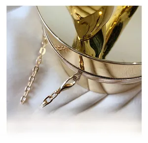 Macro detail of high-shine gold round cylinder box bag showing metallic chain hook