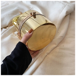 Detail of a golden cylindrical acrylic box bag with reflective mirror finish and chain strap