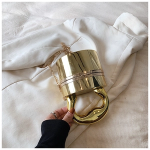Detailed top view of gold cylindrical acrylic handbag with oversized metallic handle