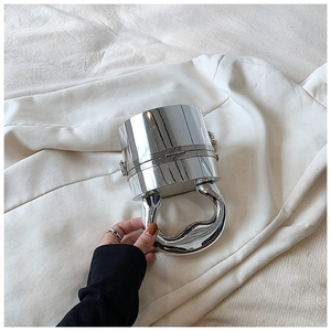 Detail of glossy silver cylindrical acrylic clutch with sculptural handle on white fabric