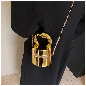Detail of glossy gold cylinder clutch with sculptural handle and metallic chain strap
