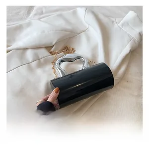 Detail of a black cylindrical bag featuring a silver heart handle and gold chain strap