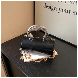 Detail of black cylindrical bag featuring a silver sculptural handle and gold chain strap