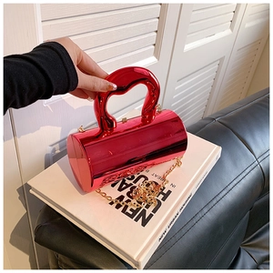 Close-up of a bright red glossy cylinder bag with sleek round handle and gold chain strap