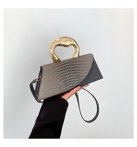 Detail of stone-patterned trapezoid bag featuring unique gold sculptural metal handle