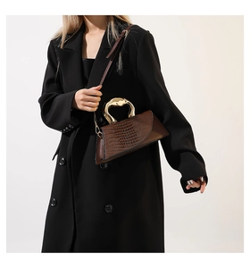 Brown crocodile embossed tote bag with gold sculpted handle worn over a black coat