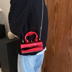 Glossy red cylinder handbag with metallic finish, unique handle, and gold chain strap