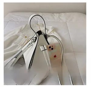Mini white triangular handbag shown next to a smartphone to demonstrate portable size