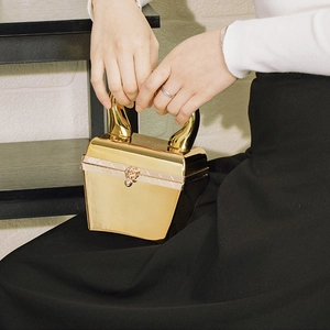 Detailaufnahme der goldenen Acryl-Clutch mit Metallic-Struktur und Griffen