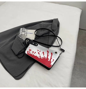 Detail of silver crossbody bag featuring realistic red blood splatter and metal studs