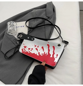Silver metallic crossbody bag with red splatter pattern on gray blazer background