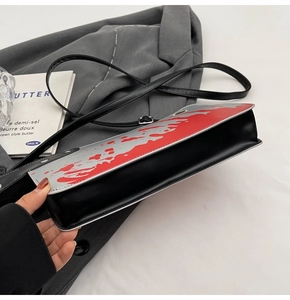 Detail view of the gusseted bottom and red splatter design on the grey PU crossbody bag