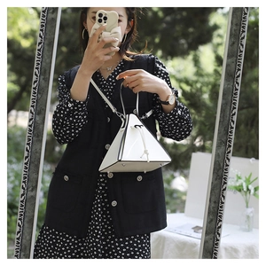 Detail of white triangle bag with black contrast trim and metal protective feet on bottom