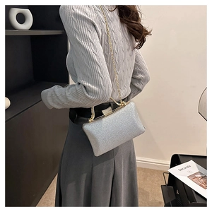 Side view of a silver sparkling evening clutch bag with golden chain on a model