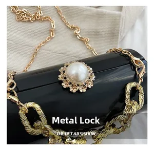 Close-up of golden hardware lock with large faux pearl and metallic chain on black bag